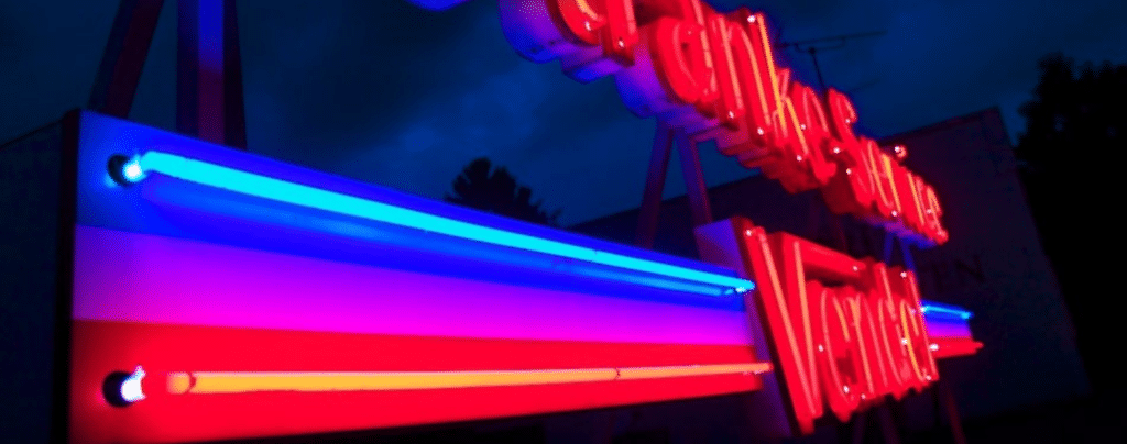 Leuchtendes Neon-Schild mit roten Buchstaben und blauen sowie roten Neonröhren vor dunklem Nachthimmel.