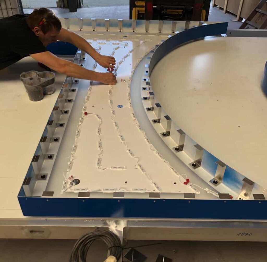 Mann arbeitet an einem großen, halbkreisförmigen Metallelement mit eingesetzten LED-Modulen in einer Werkstatt.
